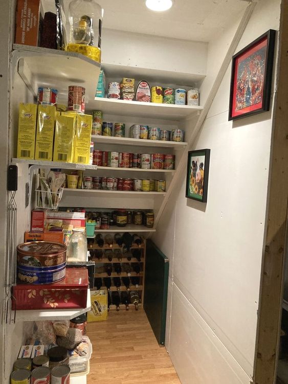 a practical staircase pantry with built-in shelves and open shelving, with tain boxes and containers plus a wine bottle stand