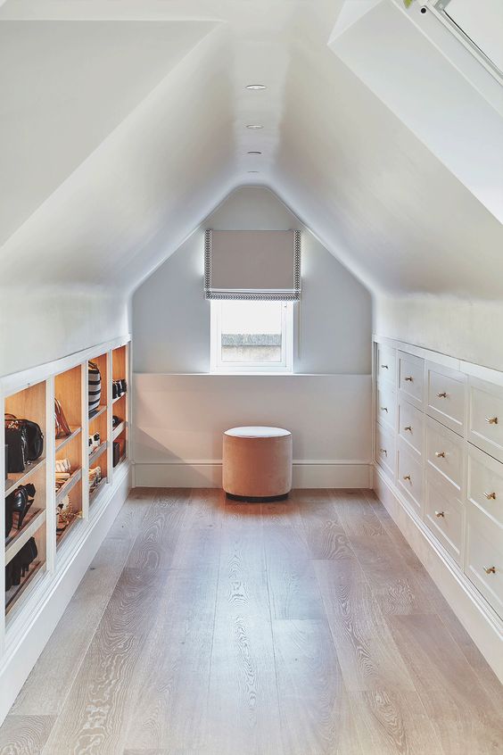 a pretty attic closet with open storage compartments and shoe shelves plus built-in drawers and a blush pouf is lovely