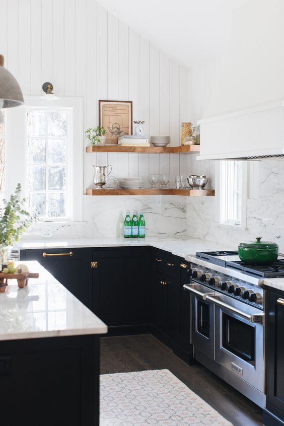 a pretty modern farmhouse kitchen with black lower cabinets and corner shelves, gold touches and a large hood