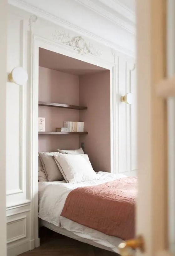 a refined French bedroom with a large niche painted dusty pink, a bed placed in there and some stained shelves and sconces