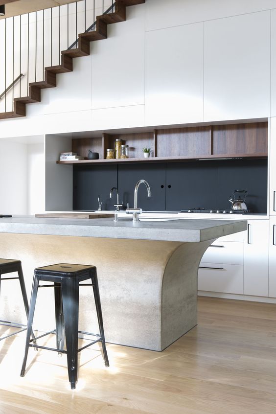 a refined contemporary kitchen with sleek cabinets built in under the stairs, with a black backsplash, a catchy kitchen island