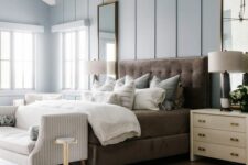 a refined modern farmhouse bedroom with blue walls, a brown bed with neutral bedding, a striped bench, neutral nightstands