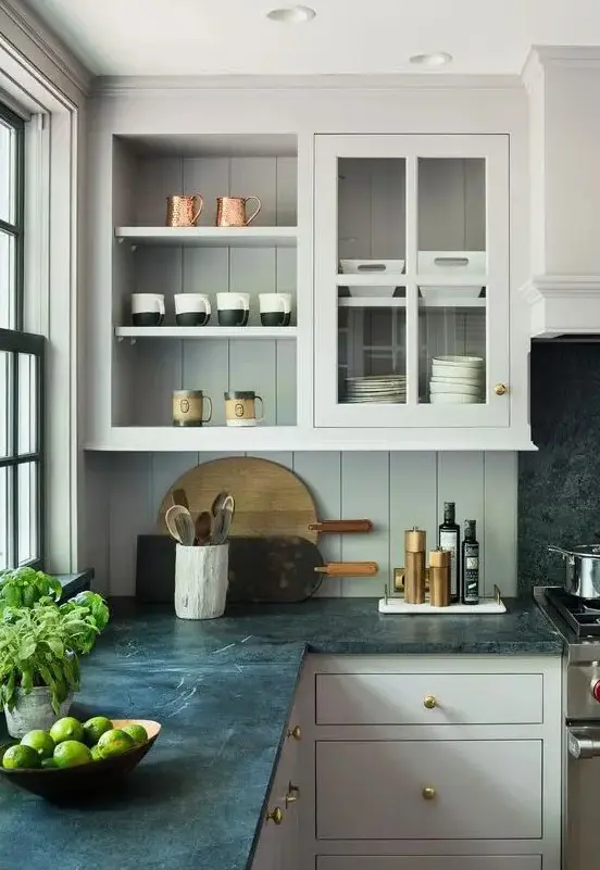 a refined neutral kitchen with usual and glass cabinets, a green beadboard backsplash and black stone countertops