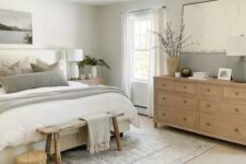 a serene modern farmhouse bedroom with an upholstered bed and neutral bedding, a stained dresser, a stained bench, some decor and a basket