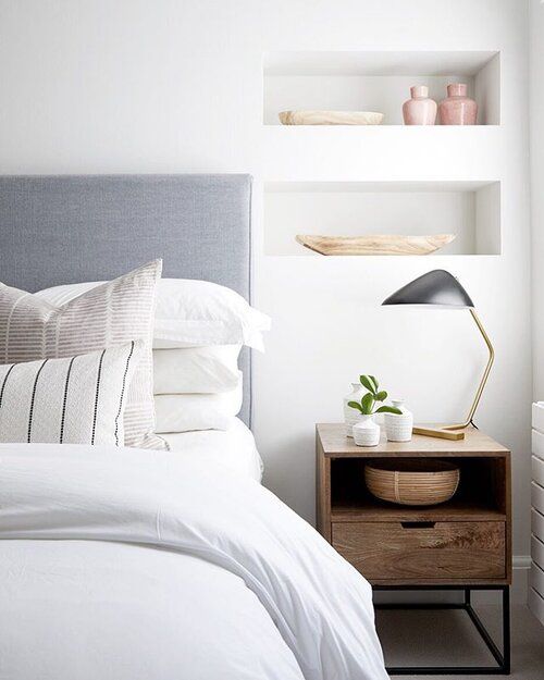 a serene neutral bedroom with a grey bed and neutral bedding, niches for decor, a stained nightstand and a black lamp