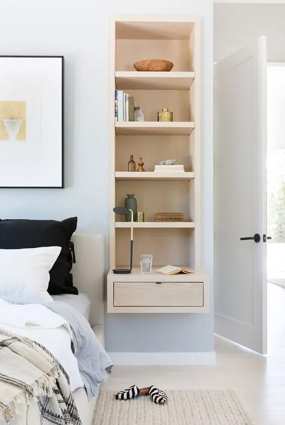 a serene neutral bedroom with pale blue walls, a bed and a niche with a built-in storage piece and a drawer, some decor and necessary stuff