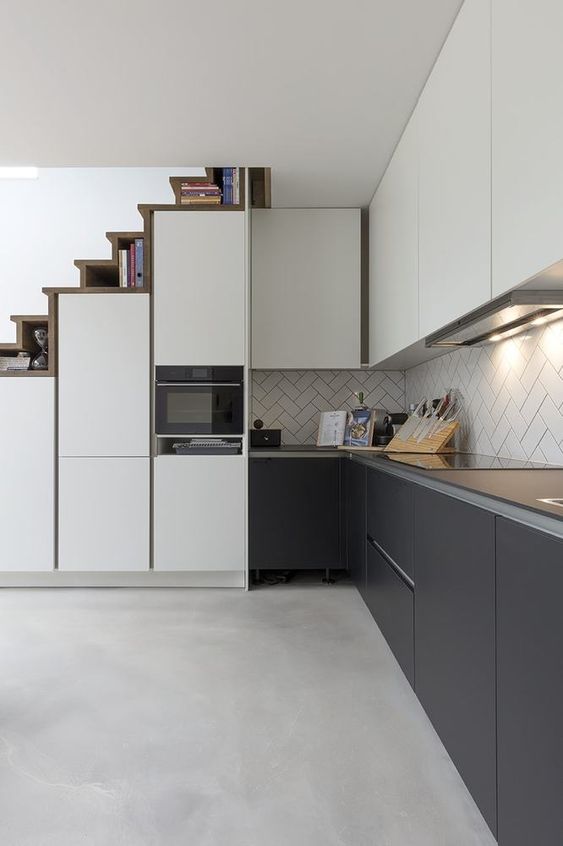 a sleek modern kitchen with upper white and lower soot cabinets, a herringbone backsplash, a staircase that hides storage compartments