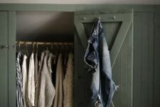 a sloped ceiling nook with green shiplap doors that hide railing for clothes is a smart solution for a farmhouse space