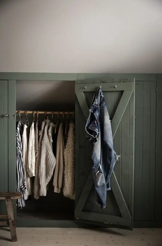 a sloped ceiling nook with green shiplap doors that hide railing for clothes is a smart solution for a farmhouse space