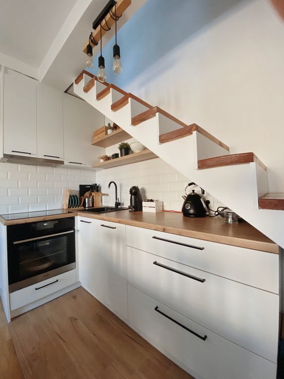a small Scandi kitchen under the stairs, with butcherblock countertops and a white brick backsplash, pendant bulbs