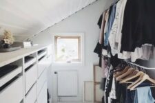 a small and cool attic closet with a dresser, railings for clothes, a printed rug and some art is a smartly organized space