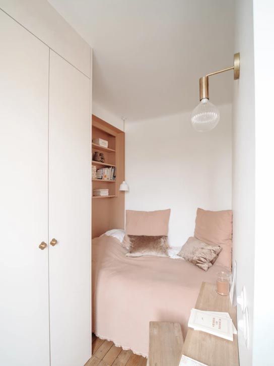 a small and cozy bedroom with a dusty pink niche with shelves instead of a usual nightstand and a small console and a stool