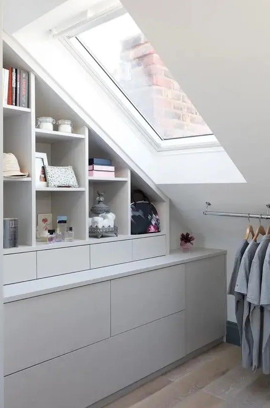 a small attic closet with open storage compartments and cabinets and drawers, a rail with clothes is a smart and cool idea