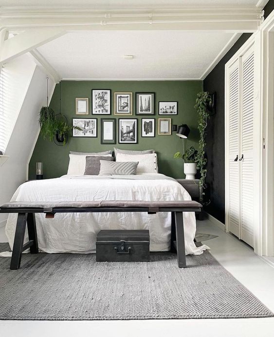 a small bedroom in neutrals, with a green accent wall, a gallery wall, a bed with neutral bedding and a black bench