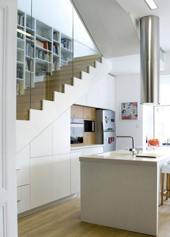 a small modern kitchen in white built in under the staircase, with a large kitchen island, a hood over it and some appliances