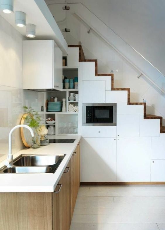 a small modern kitchen with a staircase that hides storage compartments, lower stained cabinets, a white stone countertop