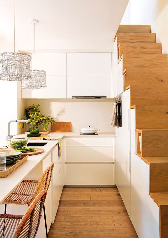 a small modern white kitchen partly built into the staircase, with a kitchen island that doubles as a dining zone