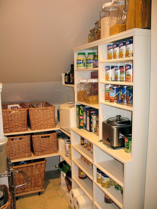 a small staircase pantry with built-in shelves and a large open storage unit, baskets and plastic and glass containers