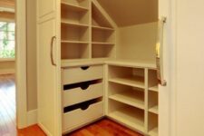 a small white attic closet with open compartments, drawers and lights is a cool idea if you have an awkward nook