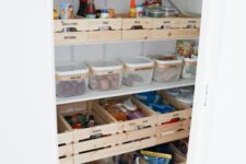 a smartly organized under stairs pantry with open shelves, wooden boxes, plastic containers and glass vessels