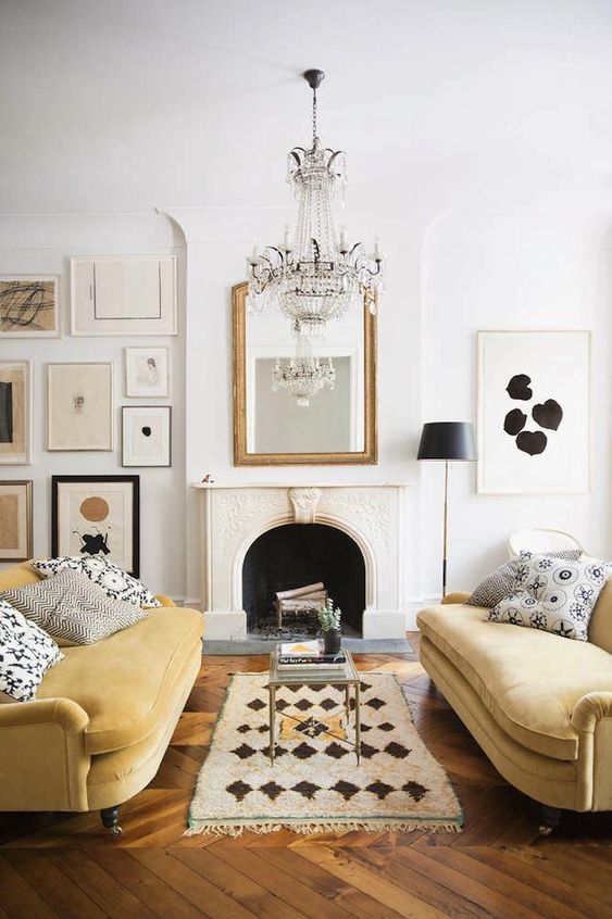a sophisticated living room with a fireplace, a printed rug, pale yellow sofas and printed pillows, a stylish gallery wall and a crystal chandelier