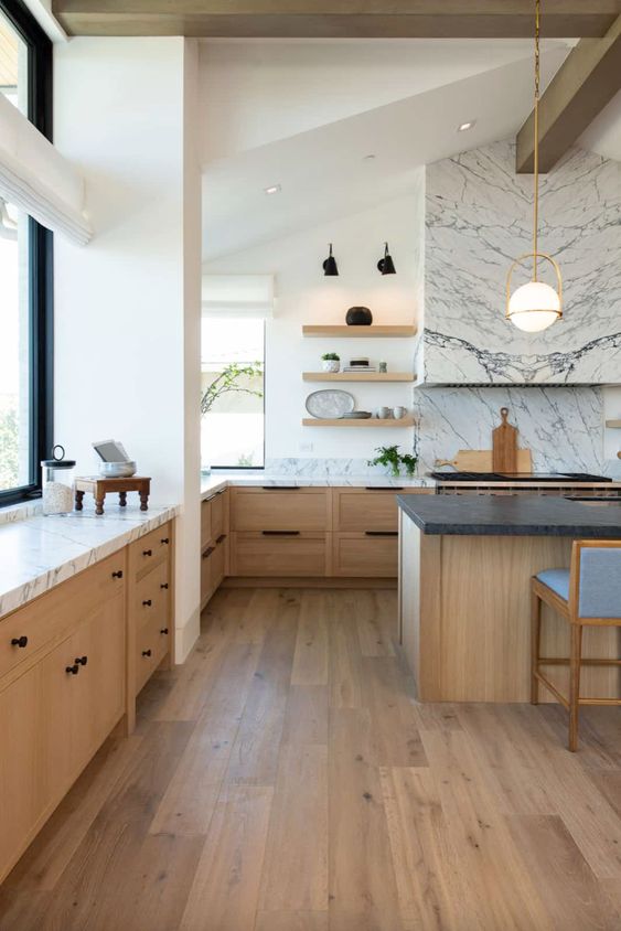 a sophisticated modern farmhouse kitchen with stained lower cabinets, a stained kitchen island, white marble countertops and a hood clad with marble