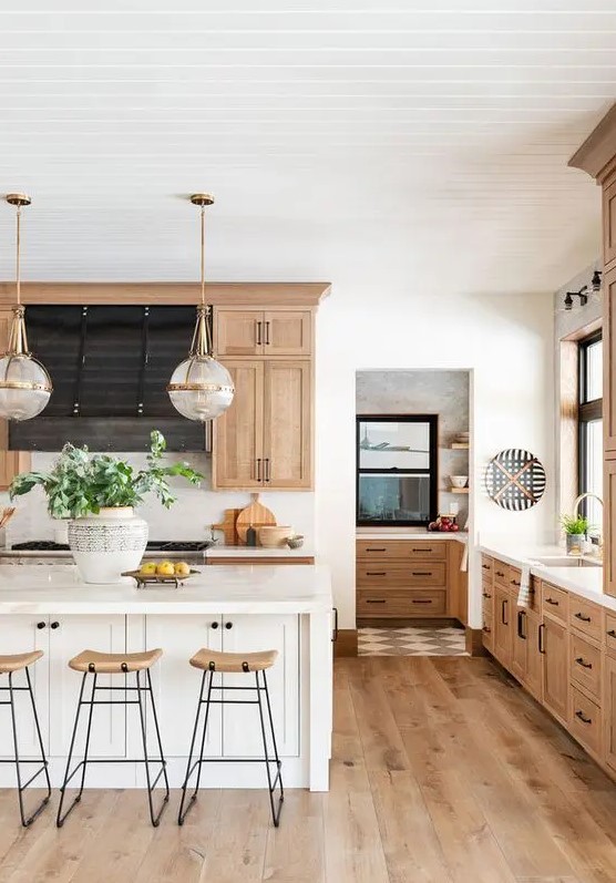 a stained modern farmhouse kitchen with a white kitchen island, tall wooden stools and pendant lamps is cozy