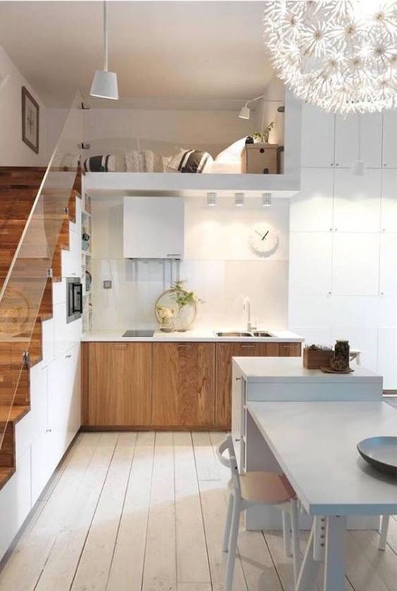 a stylish Nordic kitchen with stained lower cabinets, a staircase that hisde a lot of storage space, a white kitchen island with a table