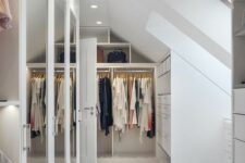 a stylish minimalist attic closet with wardrobes with mirror doors, railings, built-in drawers and built-in lights