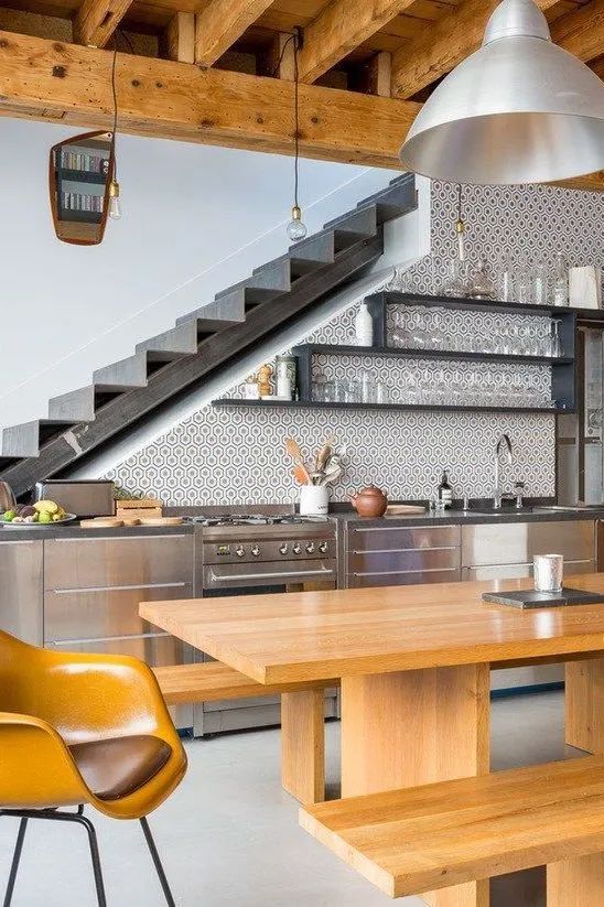 a stylish modern kitchen placed at the staircase, with metal cabinets, open shelves, a timber dining set and pendant lamps