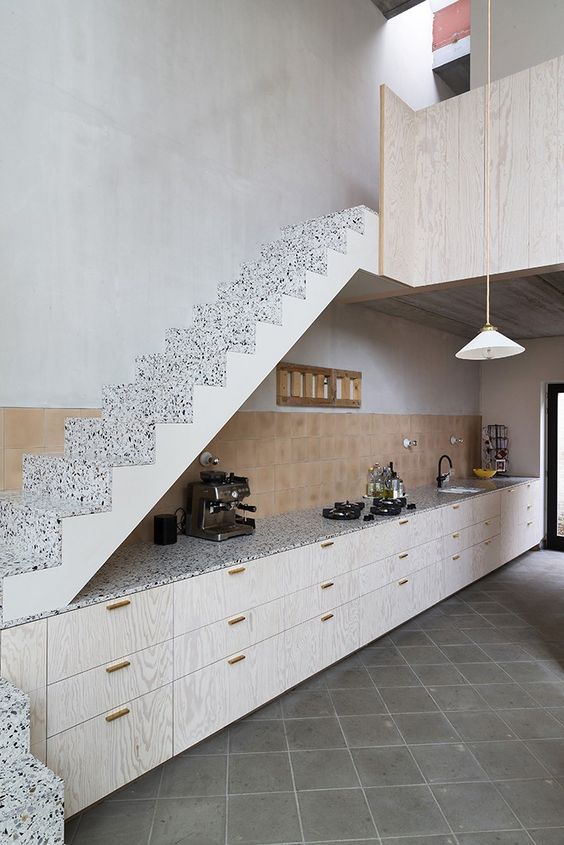 a stylish modern kitchen with whitewashed lower cabinets under the stairs, a tile backsplash and terrazzo countertops