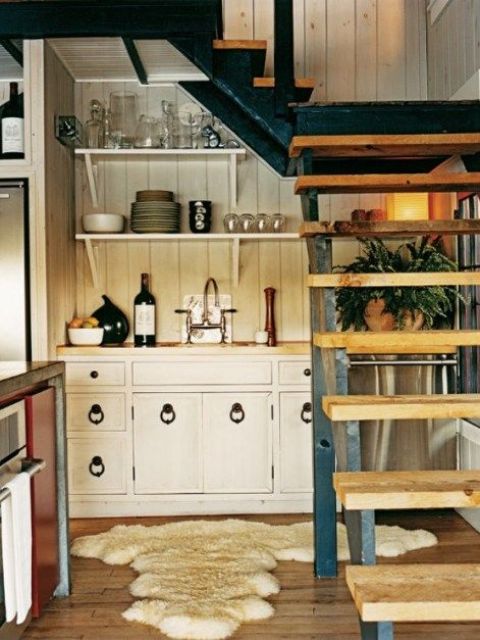 a tiny farmhouse kitchen under the stairs, with a bit of cabinetry, pulls, open shelves, a kitchen island and some greenery