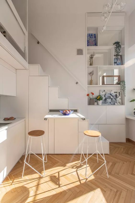 a tiny white kitchen partly built into the staircase, with a retracting table is a smart solution if you face lace of space