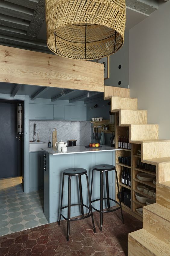 a tiny yet chic kitchen with staircase that is used for storing things, grey cabinets and a kitchen island that is a dining space, too
