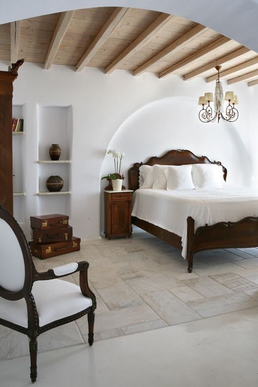a vintage bedroom with niches with shelves used for displaying vases, an arched niche with a refined bed, dark-stained furniture, a chic chandelier