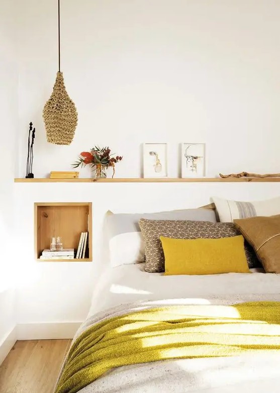 a welcoming modern bedroom with a bed, a timber niche with books and other stuff, a ledge with artwork, an arrangement and a pendant lamp