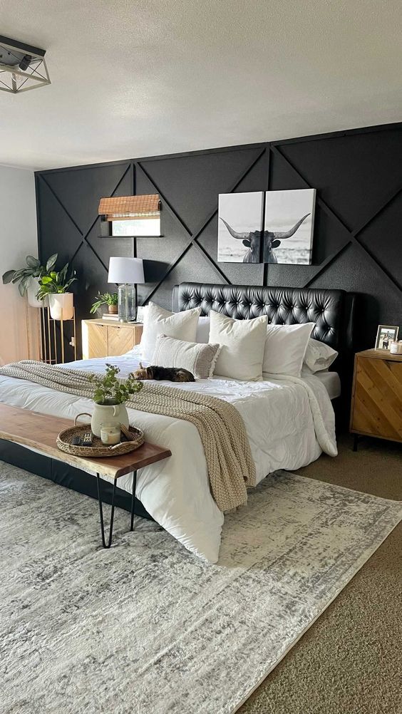 a welcoming modern farmhouse bedroom with a black paneled wall, a black bed with neutral bedding, a bench with hairpin legs and greenery