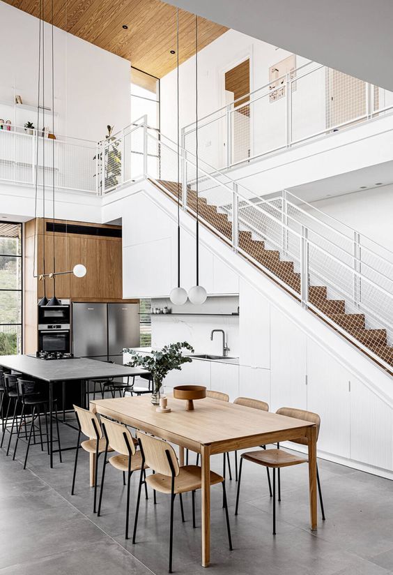 a white Scandinavian kitchen built into the staircase, with built-in appliances, a kitchen island and a dining zone