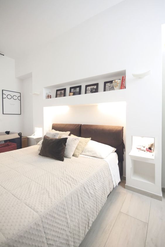 a white bedroom with some niches, a niche with lights for the bed, niches for storage and display and some other furniture