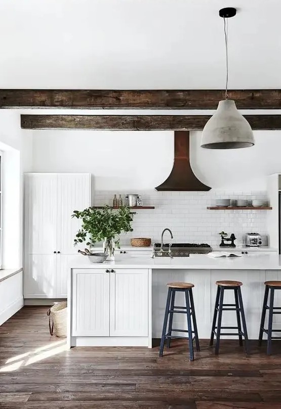 a white modern country kitchen with white planked cabinets, dark ceiling beams, pendant lamps, tall stools and shelves