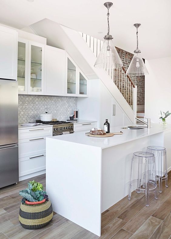 a white modern farmhouse kitchen placed under the stairs with cabinets built in, a scallop tile backsplash, a kitchen island