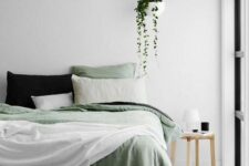 an airy Scandinavian bedroom with a bed and green bedding, a stool as a nightstand, a suspended pot with greenery