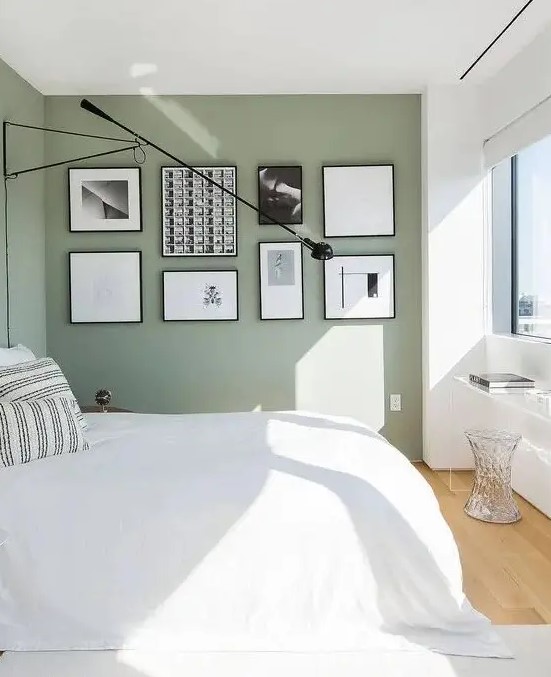 an airy Scandinavian bedroom with sage green walls, a bed with neutral bedding, a black and white gallery wall