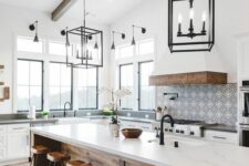 an airy modern farmhouse kitchen with lower white cabinets, a large kitchen island with a dining zone, pendant lamps and a large hood