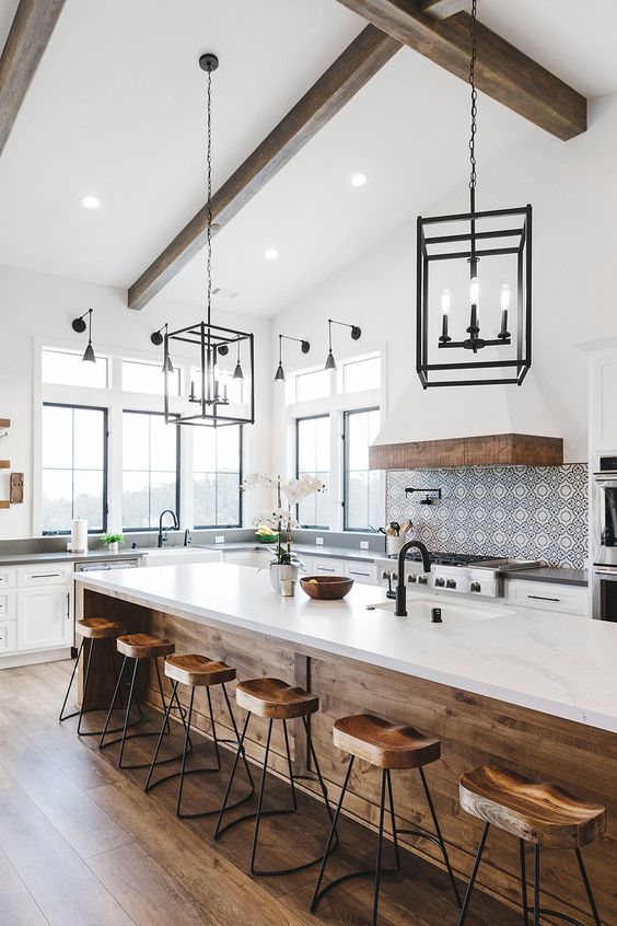 an airy modern farmhouse kitchen with lower white cabinets, a large kitchen island with a dining zone, pendant lamps and a large hood