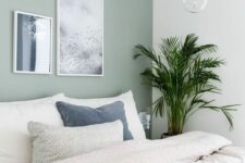 an airy neutral bedroom with a pale green accent wall, a bed withneutral bedding, a mini gallery wall and a bubble lamp