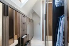 an attic closet with elegant stained built-ins with mirrors and drawers and super tall racks for hanging clothes