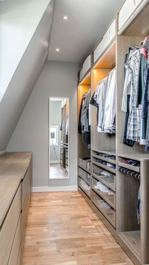 an attic closet with open storage compartments and lights, drawers and railing, several dressers and a long and tall mirror