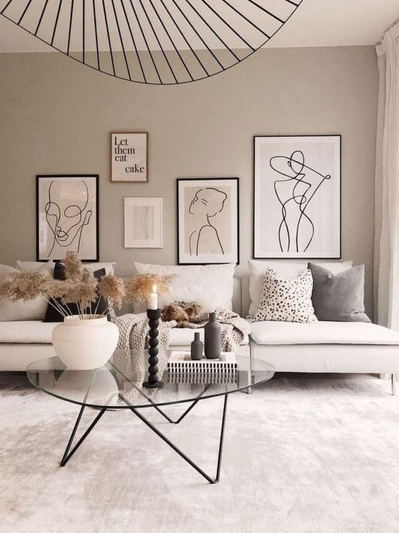an elegant neutral space with a creamy sofa, a glass coffee table, a free form gallery wall in matching colors and a cool chandelier