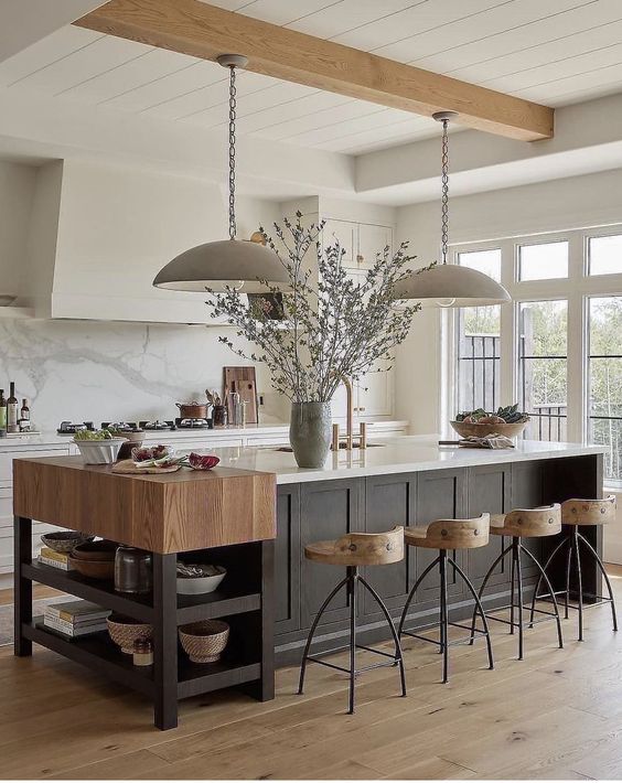 an elevated modern farmhouse kitchen with white cabinets and a black kitchen island, an additional console, wooden stools and pendant lamps